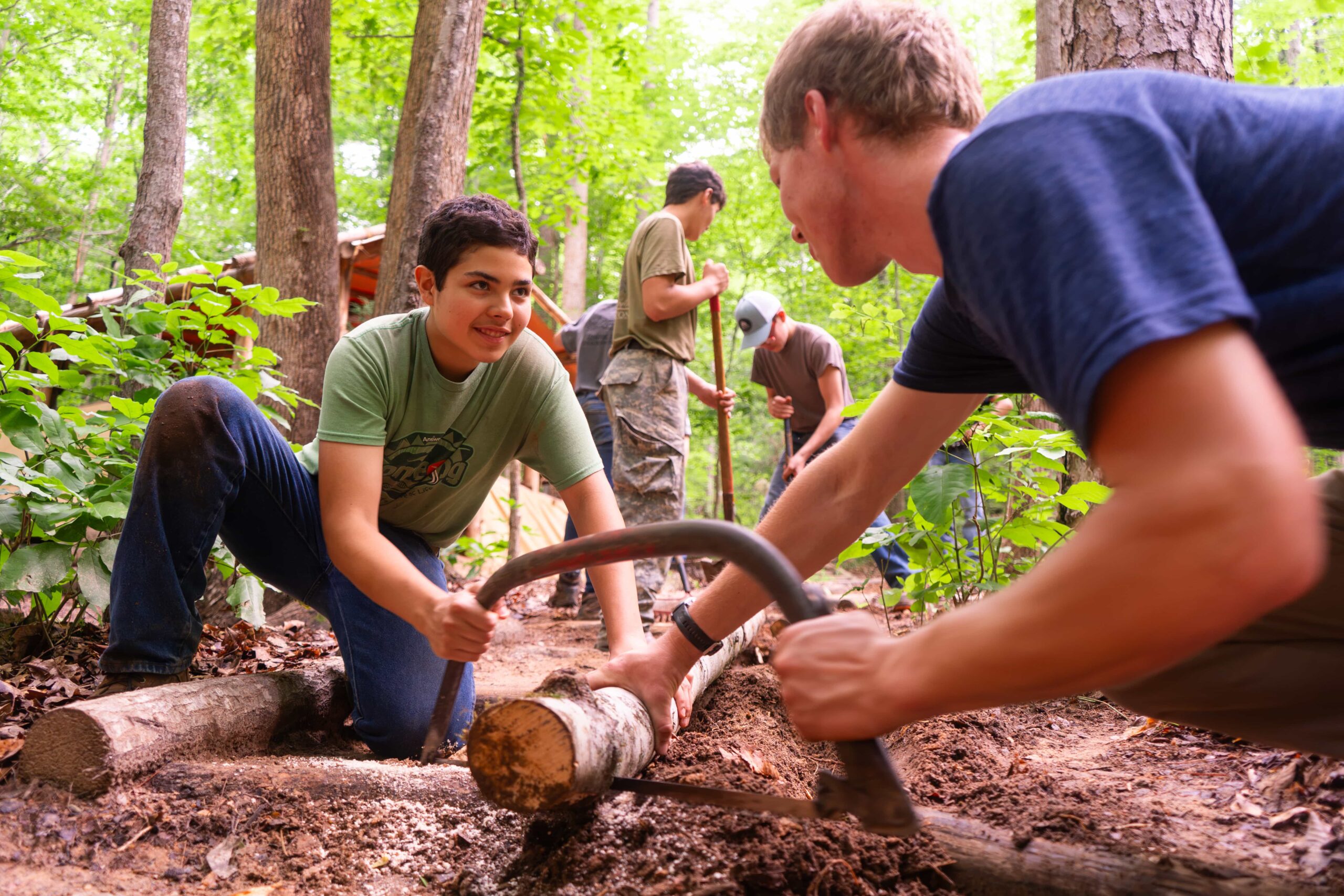 Campers and a Fair Play Chief sawing a log together in the woods
