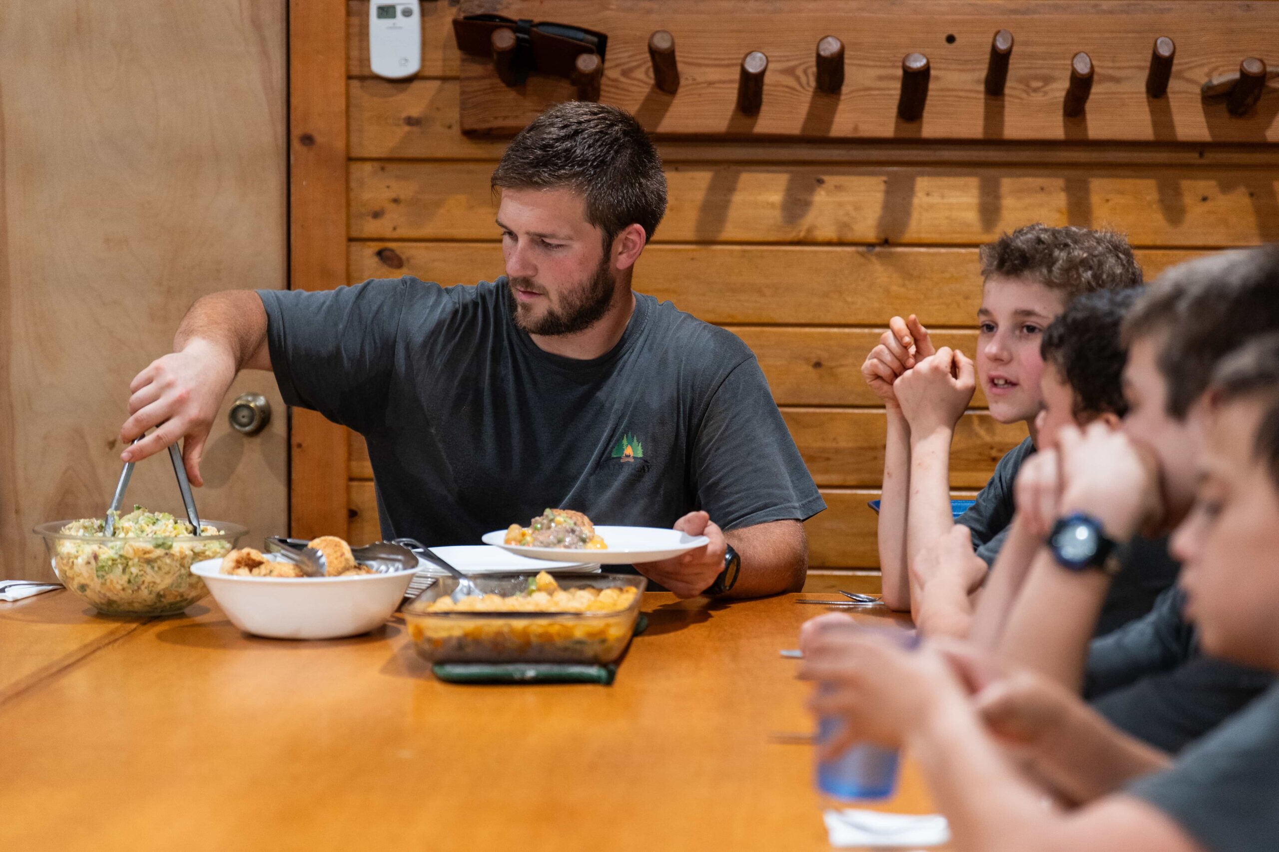 Fair Play Camp Chief serving a meal to boys gathered around a table